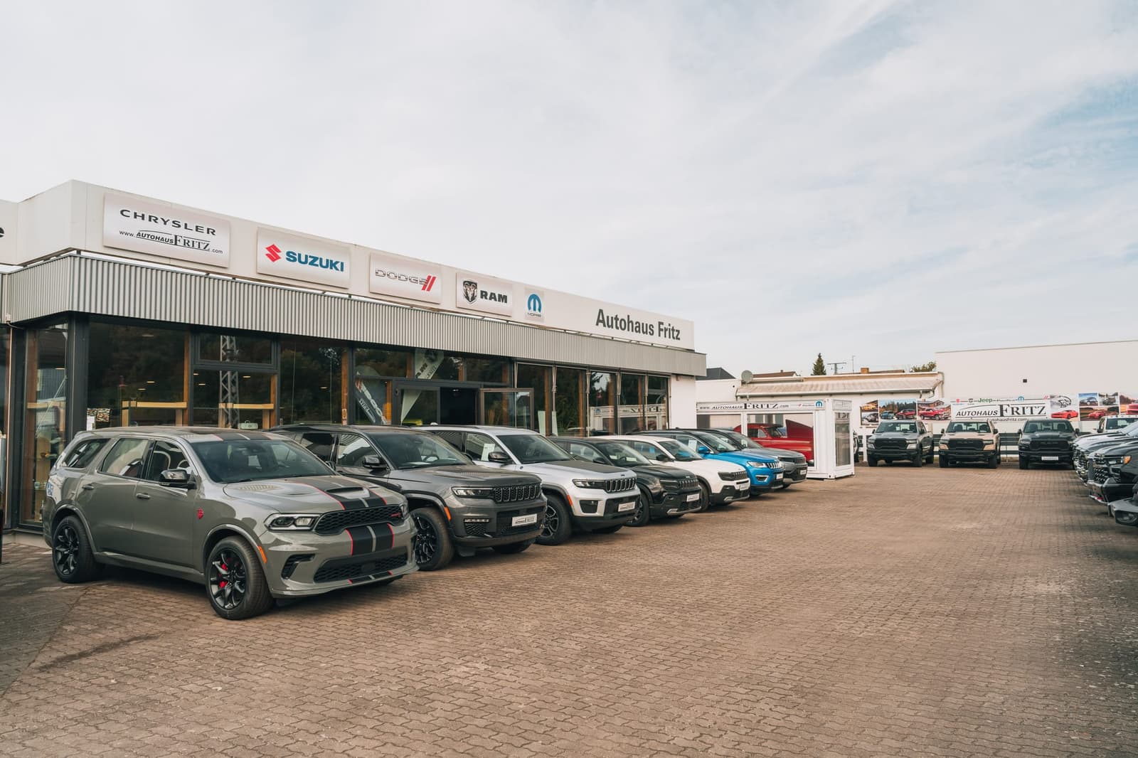 Ausstellungsgebäude von Autohaus Fritz mit Markenschildern an der Fassade, davor Fahrzeuge auf dem Hof